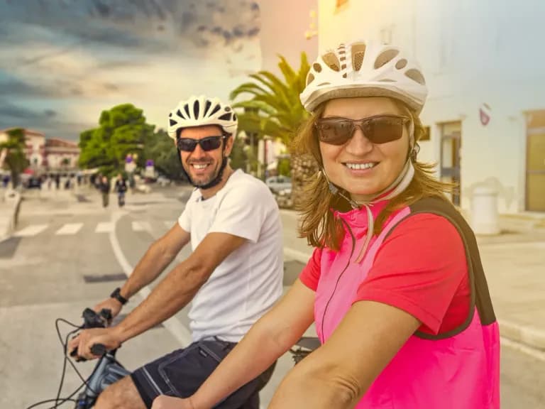 Lachendes Paar mit Helmen auf dem Rad in einem Dorf auf Mallorca