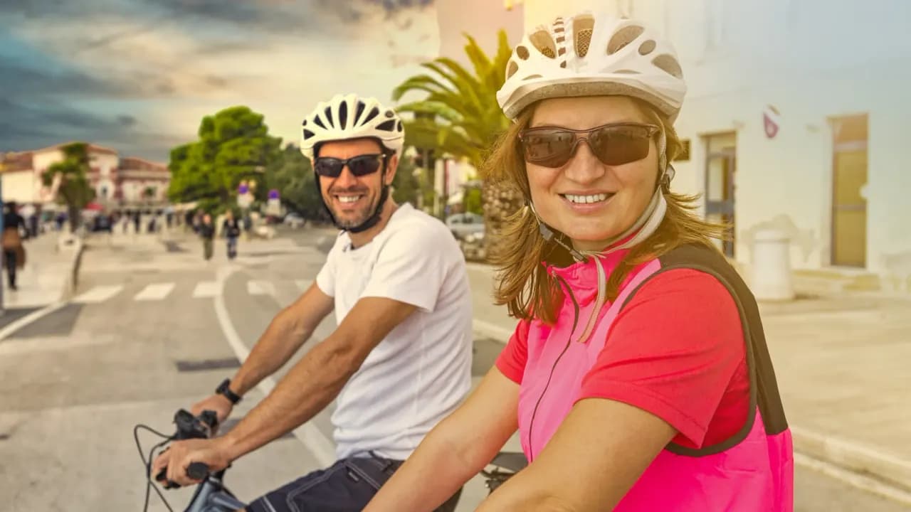 Lachendes Paar mit Helmen auf dem Rad in einem Dorf auf Mallorca